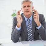 Wishing businessman crossing his fingers in his office